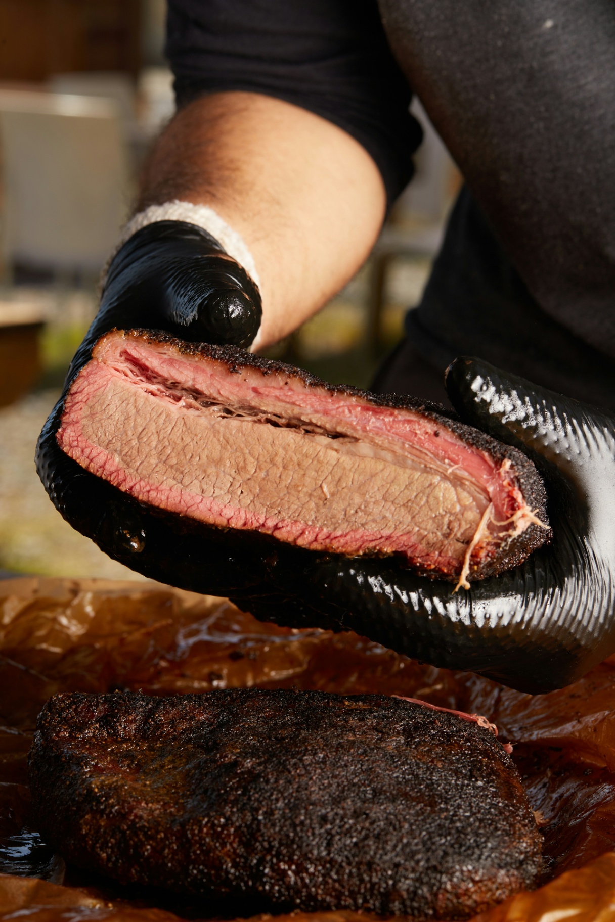 Hand-held cross-section of pepper-crusted brisket with smoke ring