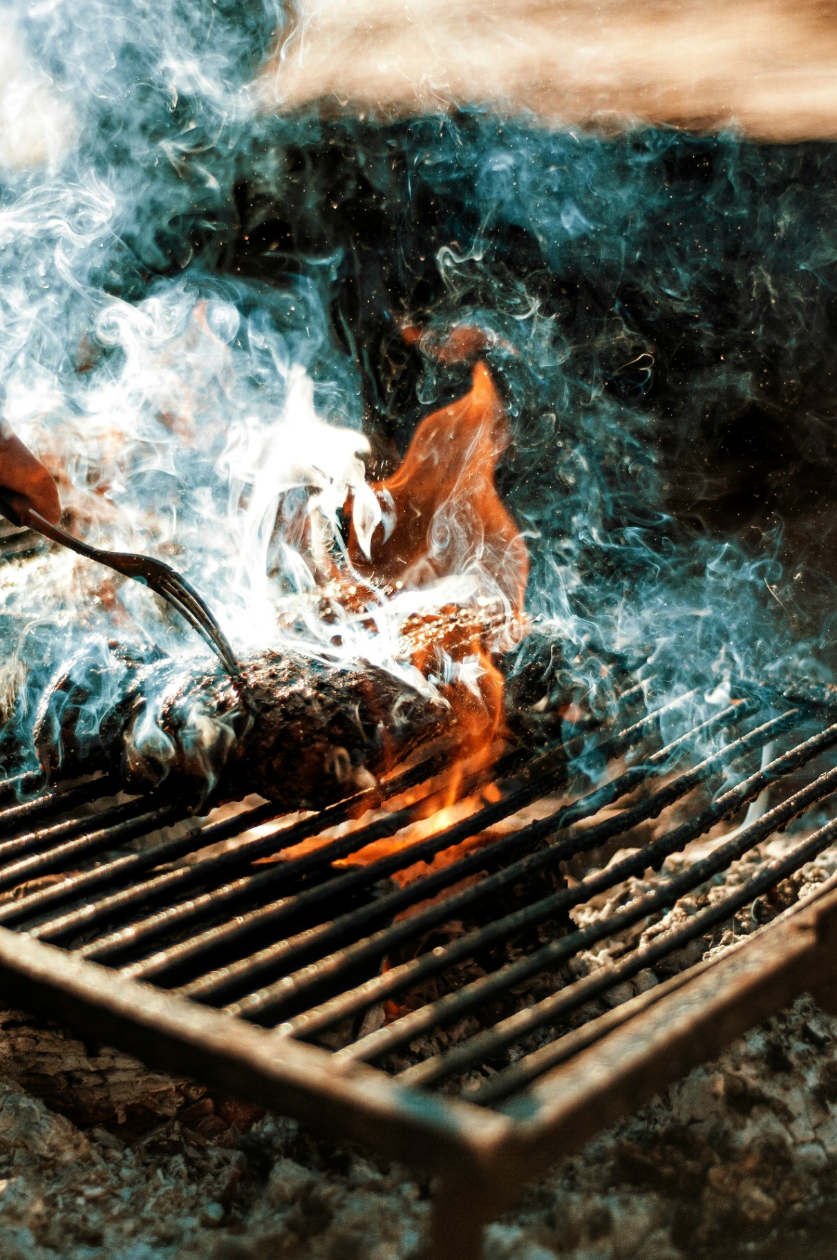 Live fire and smoke wrapping a cut of beef on the grill